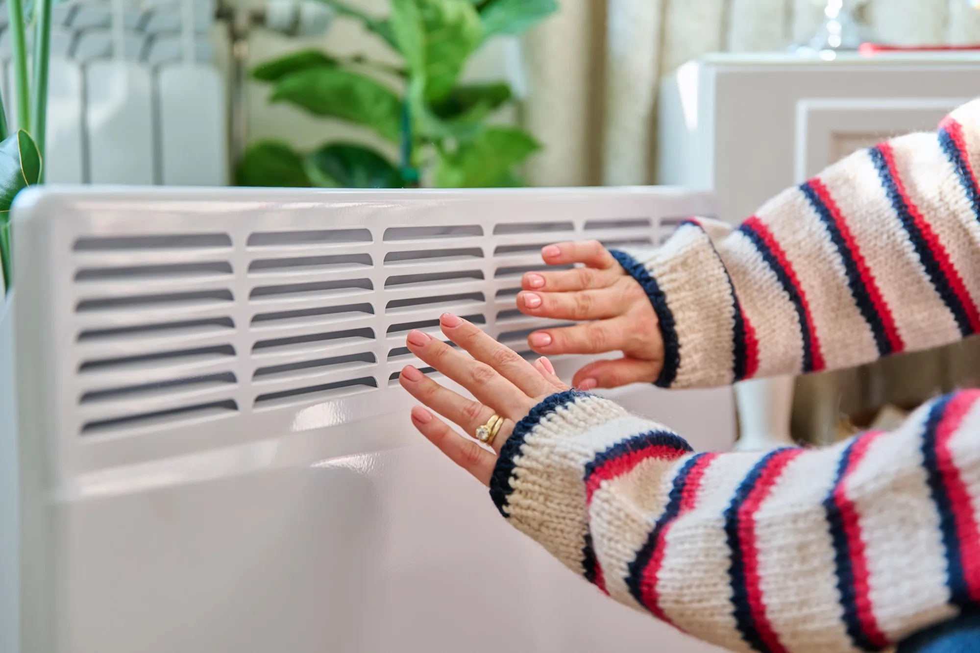 Close-up of woman hands warming near electric heating radiator